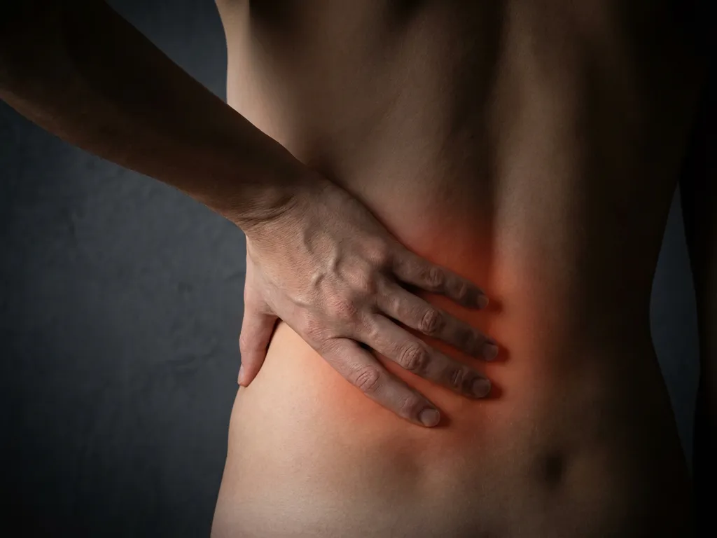 Persoon raakt onderrug aan waar rode gloed lage rugpijn visualiseert tegen donkere achtergrond