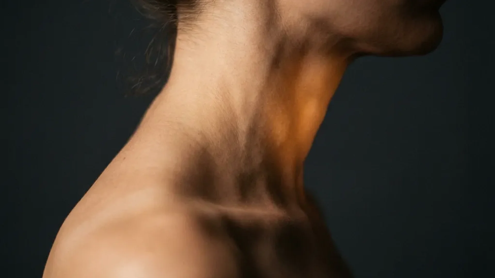 Profiel van nek en schouder met gespannen cervicale spieren en gouden therapeutische gloed, donkere achtergrond