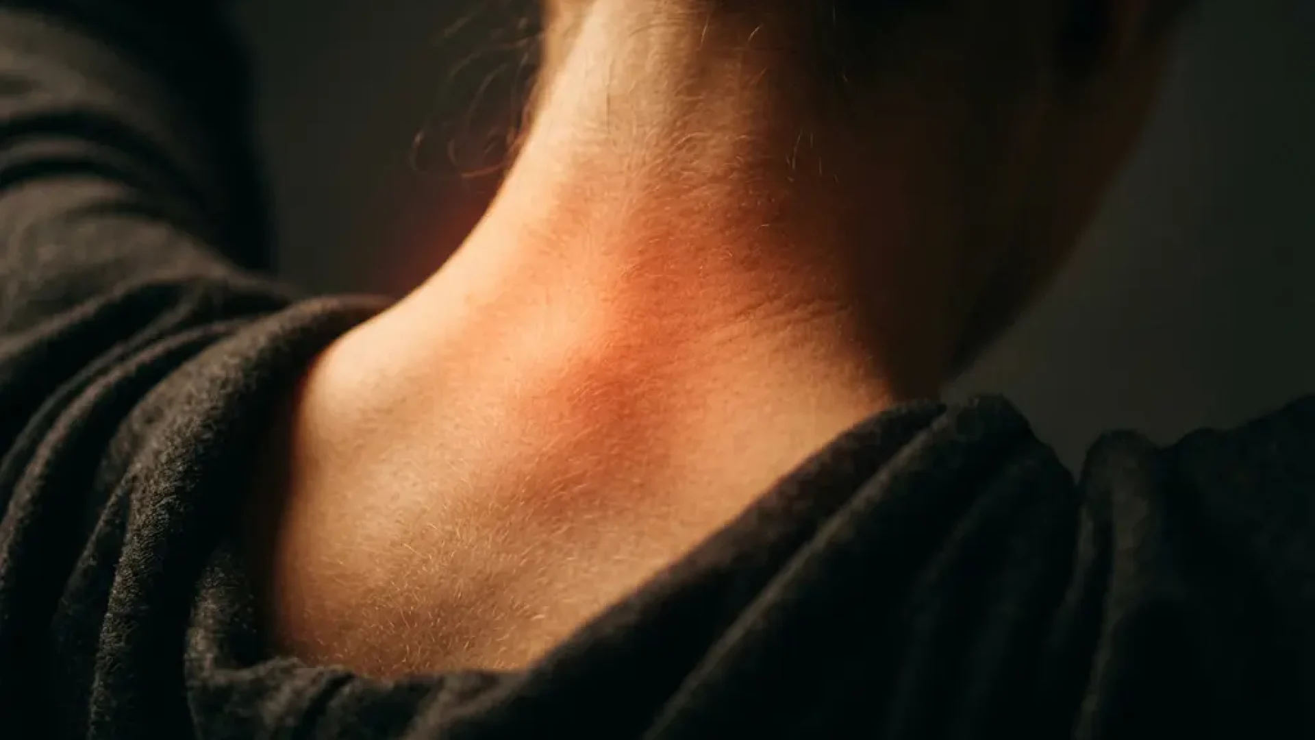 Persoon van achteren gefotografeerd met roodgloeiende pijnzone in nek en bovenrug, dramatische belichting