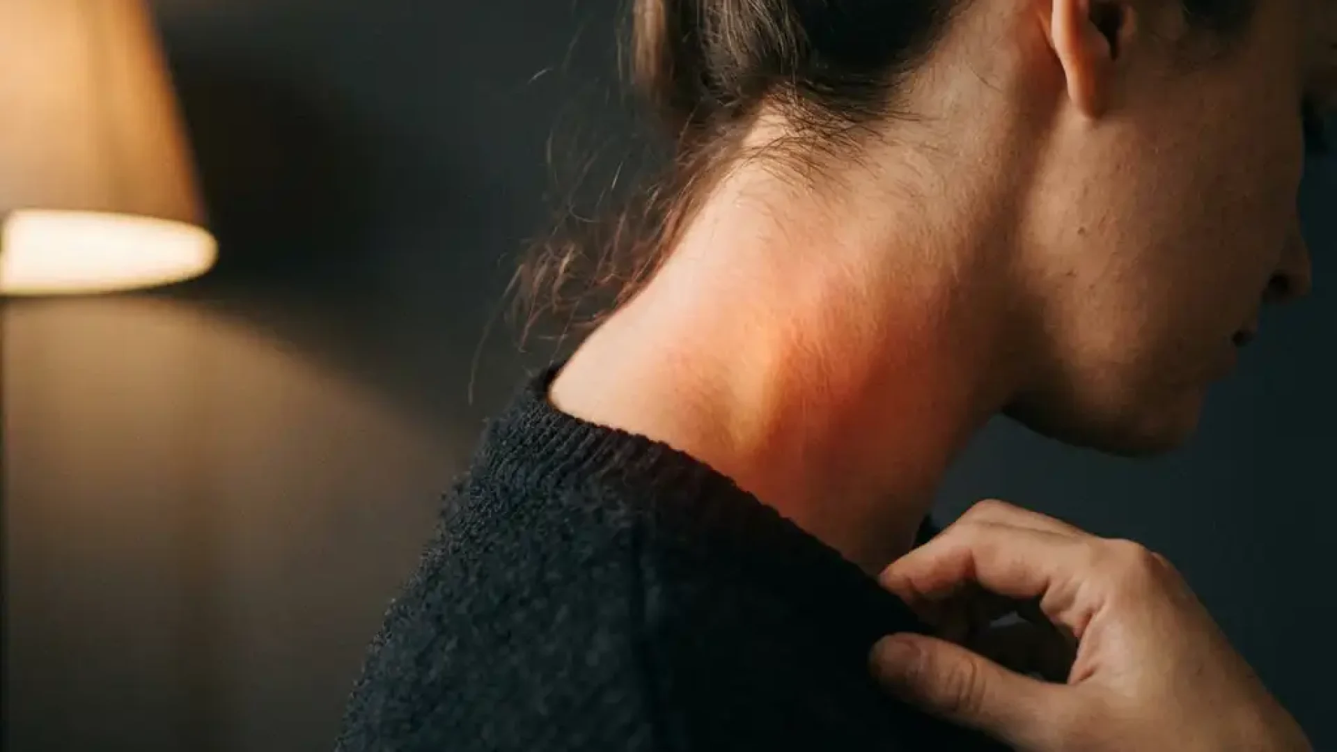 Nek en schouder van persoon met warme roodachtige gloed in cervicale wervelkolom die spanning en ongemak suggereert