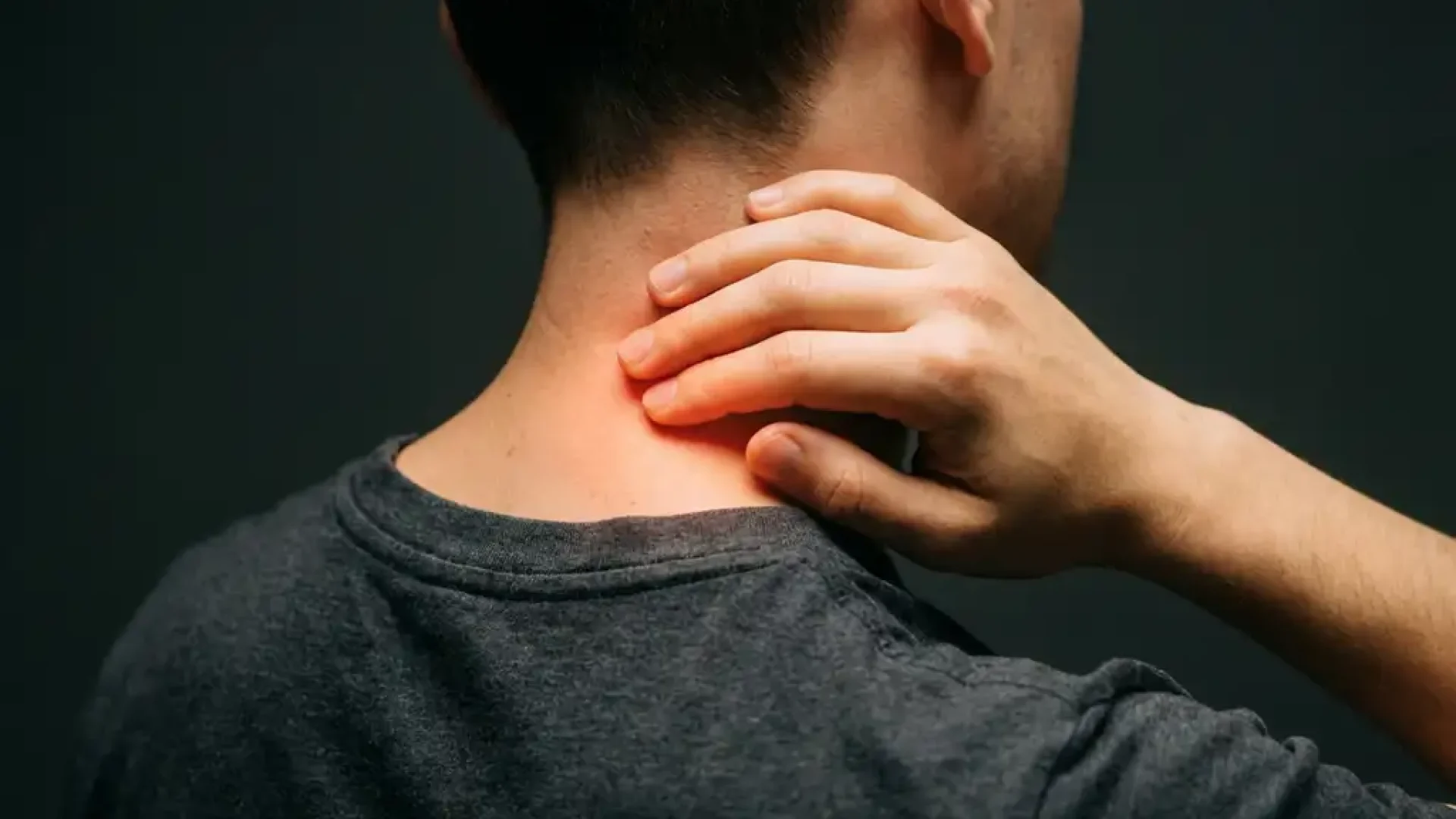 Persoon masseert nek met hand terwijl warme oranje gloed pijnverlichting toont in spierweefsel tegen donkere achtergrond