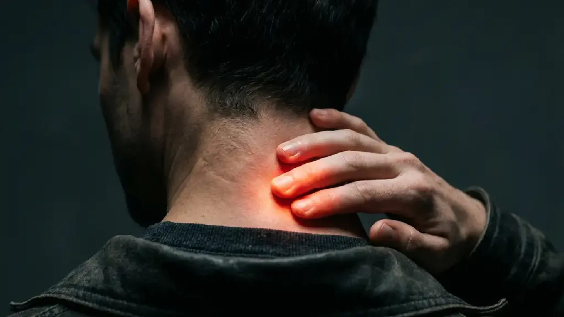 Persoon raakt nekspieren aan met vingertoppen, warme rode gloed toont spierspanning, dramatische belichting op donkere achtergrond