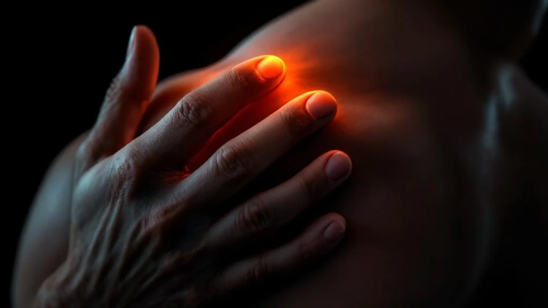 Persoon raakt pijnlijke schouder aan met dramatische oranje verlichting die spierdefiniëring en spanning benadrukt