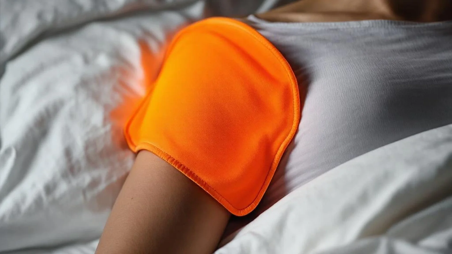 Persoon ligt op wit kussen met oranje-rode warmtekussen op schouder voor pijnverlichting en therapie